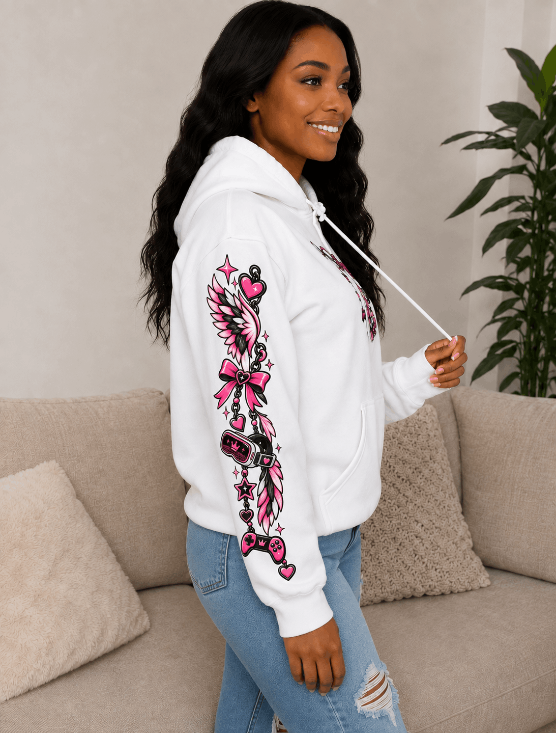 A woman wearing a white hoodie with a large pink and black graphic print on the sleeve, paired with light blue jeans, standing in a living room setting.